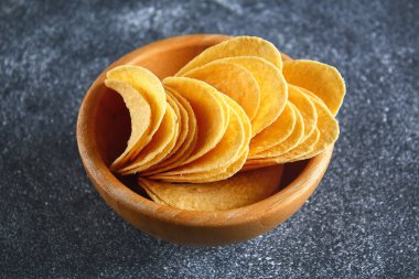 Bir gri karanlık tabloda ahşap bir kasede gevrek cipsi. Aperatif