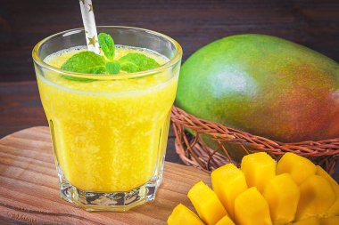 Mango ahşap bir masa üzerinde bir cam smoothies. Doğranmış mango dilimlenmiş
