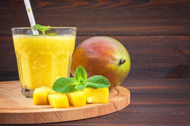 Mango ahşap bir masa üzerinde bir cam smoothies. Doğranmış mango dilimlenmiş