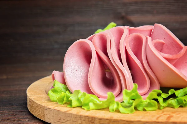Ahşap zemin üzerine salata yaprakları ile dilimlenmiş sosis.