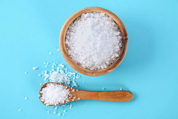 Crystals of large sea salt in a wooden bowl and spoon on a blue table