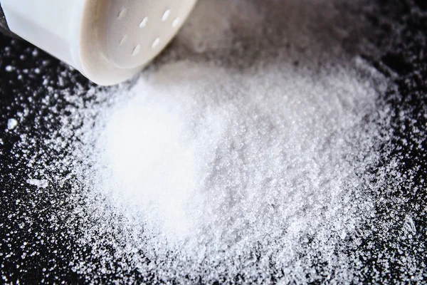 Slayt küçük kristaller tuz siyah bir tablo üzerinde dağınık vardır. Reklam tuz için arka plan. Tablo tuzlu. Tuzlanmış gıda