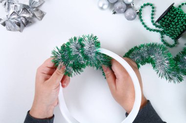 DIY Noel çelenk. Fotoğrafta bir plastik tabak, tinsel, boncuk, yay ve topları kendi elleriyle bir Noel çelenk yapmak nasıl Kılavuzu. El yapımı dekor. Gümüş yeşil çelenk. Üstten görünüm