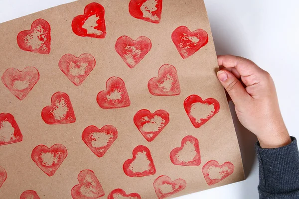 Diy. Gift wrapping for Valentine\'s Day. Kraft paper gift and potato stamp in the shape heart and red paint do it yourself on February 14th. Top view on a white background. step by step. Handicraft