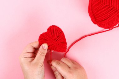 Karton, iplik pembe bir arka plan üzerinde kırmızı el yapımı DIY kalpler yaptım. Hediye fikirleri Sevgililer günü, gün aşk, 14 Şubat kavramı. Adım adım. el sanatları işlemek. Sevgililer günü kartı