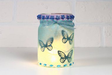 Beyaz tuğlalı arka planda Diy Peri Kavanozu. Hediye fikirleri, dekorasyon St. Şubat 14, Sevgililer Günü, aşk, düğün. El yapımı lamba, gece lambası, cam kavanozdan fener, peçete, yapıştırıcı, sim.