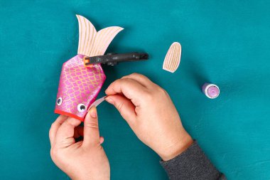 Mavi yeşil arka planda Diy koi sazan balığı. Çin yeni yılı için hediye fikirleri, dekor. Çocuk el yapımı. Sazan balığı kağıdı, tuvalet kağıdı, şaşı gözler. Adım adım. Çocuk işçiliğini işleyin. Üst görünüm.