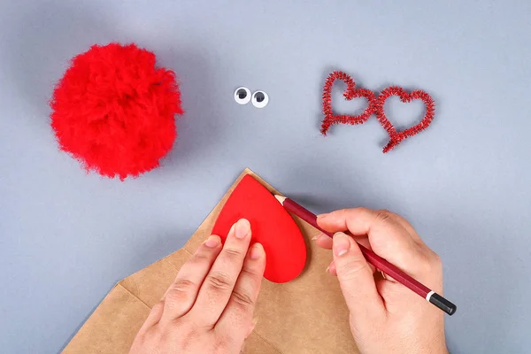 Red handmade diy monster pom pom from yarn, chenille stems in shape heart. Gift ideas for Valentines Day, day of love, the concept of February 14. Step by step. Process of kid crafts. Top view.