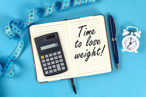 Healthy lifestyle concept with notepad. Weight loss or diet concept. Calculator, clock, measure tape on a blue table background with copy space for design. Top view.