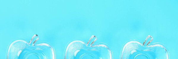 Banner. Glass cups for honey in the form of apples on a pastel of blue background. Rosh Hashanah