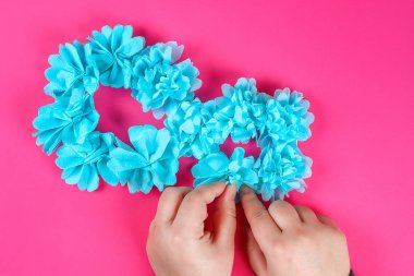 DIY sekiz yapılmış karton dekore edilmiş yapay çiçek mavi dokulu kağıt peçete pembe arka plan yaptı. Hediye fikri, dekor Uluslararası Kadınlar günü, Mart 8. Adım adım. Üstten görünüm. Süreci çocuk zanaat.