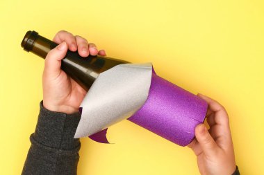 DIY Mardi Gras şişe mor kendinden yapışkanlı kağıt, yeşil boncuk, karnaval maskesi, payetler sarı arka plan. Hediye fikri, dekor Mardi Gras, yağ, Shrove Salı. Adım adım. Üstten görünüm. İşlem çocuk zanaat