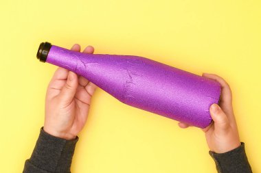 DIY Mardi Gras şişe mor kendinden yapışkanlı kağıt, yeşil boncuk, karnaval maskesi, payetler sarı arka plan. Hediye fikri, dekor Mardi Gras, yağ, Shrove Salı. Adım adım. Üstten görünüm. İşlem çocuk zanaat