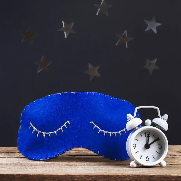 Sleeping mask handmade made of felt, stars on a black background. Kid craft. Children diy. White alarm clock showing midnight, 12 hours.