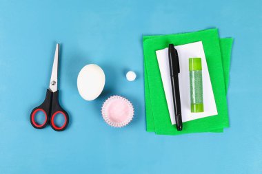 DIY tavşan yumurta üzerinde mavi arka plan çıkarma. Hediye fikirleri, dekorasyon Paskalya, Bahar. El yapımı. Beyaz Paskalya yortusu yumurta bunny, çim krep kağıt, kek cupcake fincan. Adım adım. Süreci çocuk el sanatları. Üstten Görünüm.