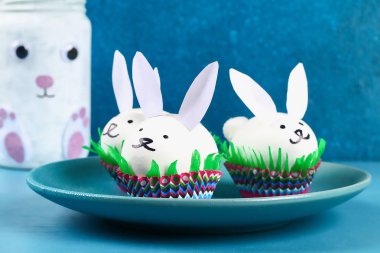 DIY tavşan yumurta üzerinde mavi arka plan çıkarma. Hediye fikirleri, dekorasyon Paskalya, Bahar. El yapımı. Beyaz Paskalya yortusu yumurta bunny, çim krep kağıt, kek cupcake fincan. Adım adım. Süreci çocuk el sanatları.