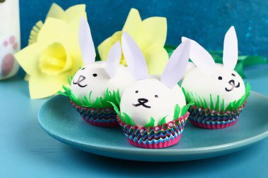 DIY tavşan yumurta üzerinde mavi arka plan çıkarma. Hediye fikirleri, dekorasyon Paskalya, Bahar. El yapımı. Beyaz Paskalya yortusu yumurta bunny, çim krep kağıt, kek cupcake fincan. Adım adım. Süreci çocuk el sanatları.