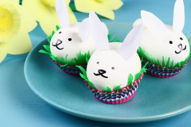 DIY tavşan yumurta üzerinde mavi arka plan çıkarma. Hediye fikirleri, dekorasyon Paskalya, Bahar. El yapımı. Beyaz Paskalya yortusu yumurta bunny, çim krep kağıt, kek cupcake fincan. Adım adım. Süreci çocuk el sanatları.