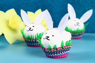 DIY tavşan yumurta üzerinde mavi arka plan çıkarma. Hediye fikirleri, dekorasyon Paskalya, Bahar. El yapımı. Beyaz Paskalya yortusu yumurta bunny, çim krep kağıt, kek cupcake fincan. Adım adım. Süreci çocuk el sanatları.