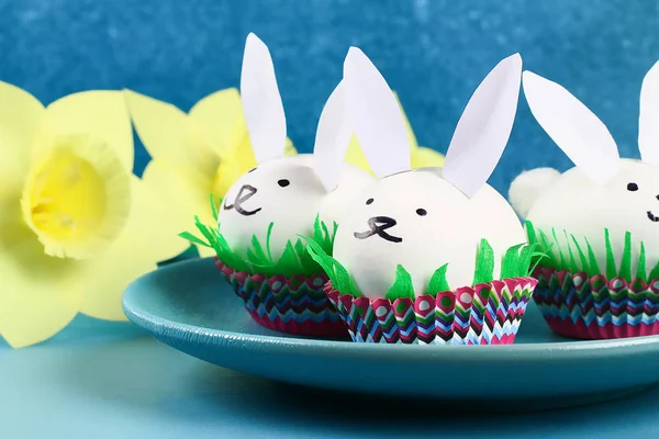 Diy rabbit from easter eggs on blue background. Gift ideas, decor Easter, spring. Handmade. White easter egg bunny, grass crepe paper, cup muffin cupcake. Step by step. Process kid crafts.