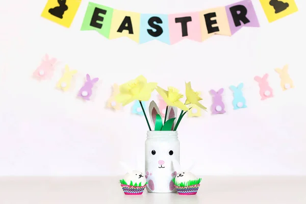 Dekor für Ostern. Papiergirlanden, Vasenhasen, Narzissen, Eier Hasen, Korb mit bemalten Eiern — Stockfoto