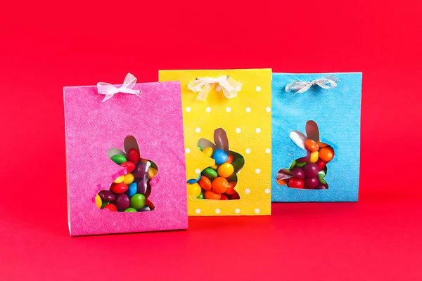 Diy Easter wrapping package sweets in a bag with a cut out bunny silhouette on a red background.