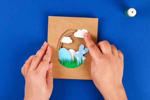DIY påsk kort från papper. Volym gratulationskort med en kanin, ägg på blå bakgrund. 3D. — Stockfoto