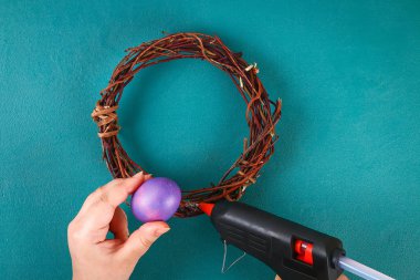 DIY Paskalya çelenk twigs, boyalı yumurta ve yeşil bir arka plan üzerinde yapay çiçekler.