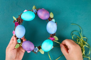 DIY Paskalya çelenk twigs, boyalı yumurta ve yeşil bir arka plan üzerinde yapay çiçekler.