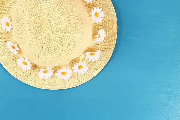 หมวกฟางที่มีดอกคาโมไมล์บนพื้นหลังสีฟ้า ท็อปวิว ประวัติฤดูร้อน แบนวาง . — ภาพถ่ายสต็อก