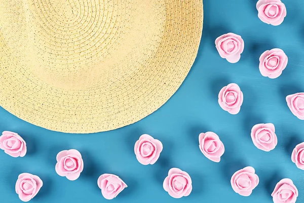 Sombrero de paja con pequeñas rosas sobre fondo azul. Vista superior. Fondo de verano. Puesta plana . — Foto de Stock