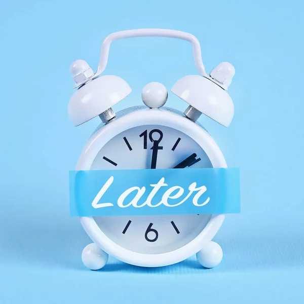 Procrastinación, retraso, concepto de urgencia. Reloj despertador blanco con una nota adhesiva con texto posterior . —  Fotos de Stock