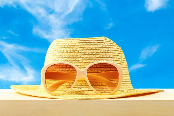 Gafas de sol amarillas y sombrero sobre estante de madera sobre fondo azul cielo. Minimalismo . — Foto de Stock