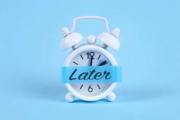 Amânarea, întârzierea, conceptul de urgenţă. Ceas deșteptător alb cu o notă lipicioasă cu text mai târziu . — Fotografie, imagine de stoc