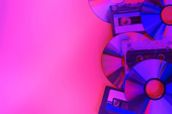 CD disks and audio cassettes on pink neon background. Minimalism.