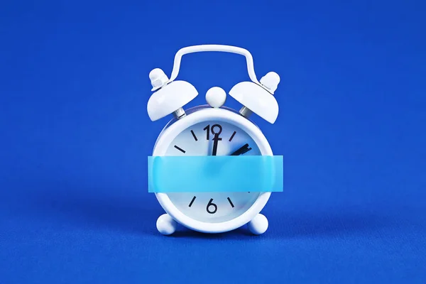 Λευκό ξυπνητήρι μπλε φόντο. Κενή αυτοκόλλητη σημείωση στο ρολόι. Αντίγραφο χώρου. Ελάχιστη έννοια. — Φωτογραφία Αρχείου