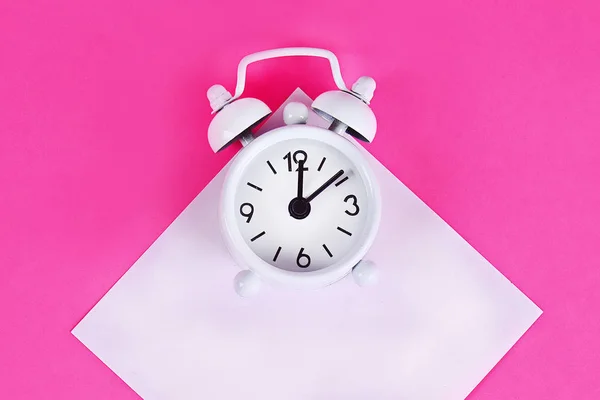 Reloj despertador blanco fondo pastel rosa. Nota pegajosa en blanco en el reloj. Copia espacial. Concepto mínimo . —  Fotos de Stock