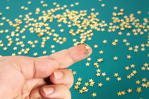 Hand touches solid confetti in the form stars. The concept of touch, tactility, feelings.