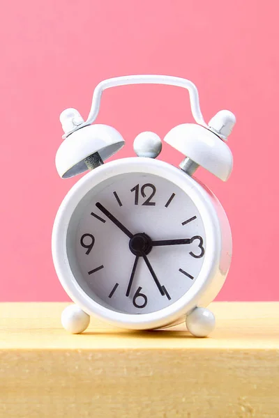 Pequeño reloj despertador blanco sobre un estante de madera sobre fondo rosa pastel. Minimalismo . —  Fotos de Stock
