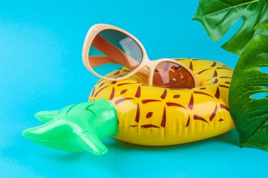 Mavi arka planda şişirilebilir ananas güneş gözlüğü ve canavar yapraklı..