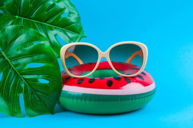 Mavi arka planda, güneş gözlüğü ve canavar yapraklı şişme karpuz. Yaz tatili konsepti. Satılık arkaplan.