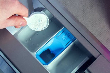 Bir adam sabun tozu döker, saç kremi döker, çamaşır makinesinin tepsisine renk katar..