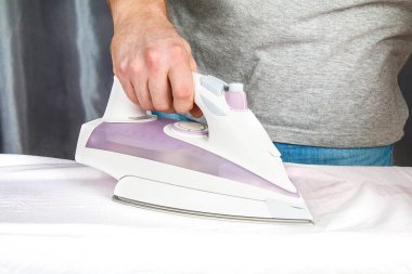 Ütü masasında siyah elektrikli ütüyle çamaşır okşayan bir adam. Ev..