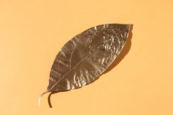 Leaves painted in gold on an orange background. Golden autumn concept.