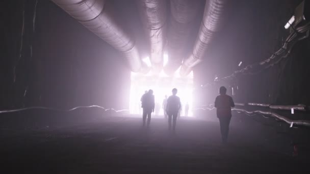 Silhouette of many construction workers walking out from a large tunnel — Stock Video