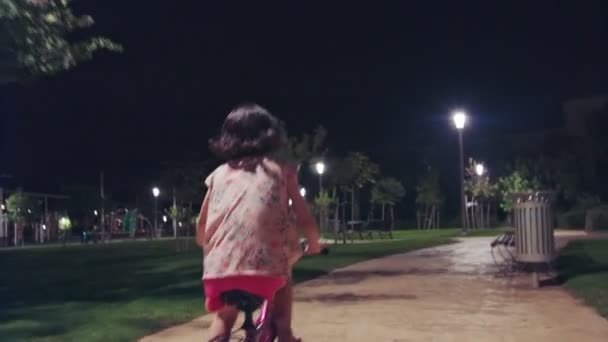Liten flicka ridning hennes cykel i en park på natten — Stockvideo