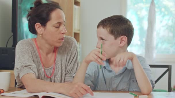 Мама помогает сыну делать уроки дома. — стоковое видео