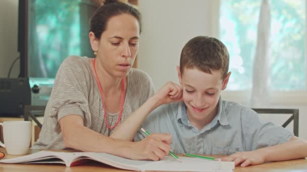 Мати допомагала їй сина, щоб зробити свою домашню роботу на дому — стокове відео