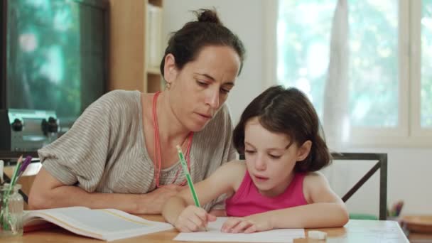 Madre ayudando a su hijita a preparar la tarea en casa — Vídeos de Stock