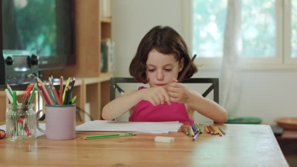 Молода дівчина сидить за столом малює кольоровими олівцями — стокове відео